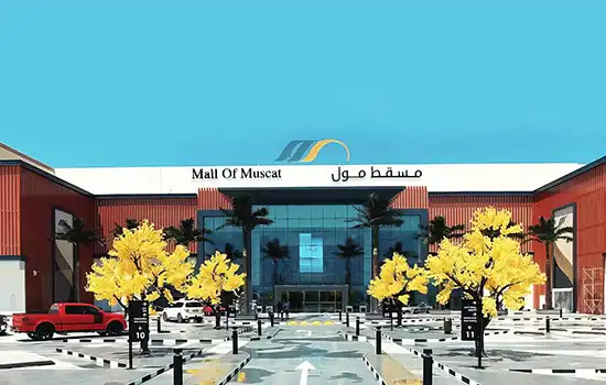 View of the entrance to Mall of Muscat in Maabela, featuring yellow trees and modern architecture.